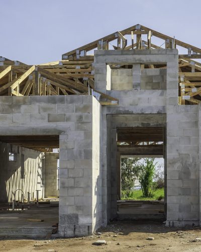 Street view of the concrete shell of a single-family house under construction, with the wooden framework of a roof in progress, in a suburban residential development in southwest Florida